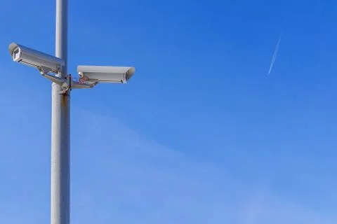 Two security cameras against the blue sky are monitoring. Stock Photos