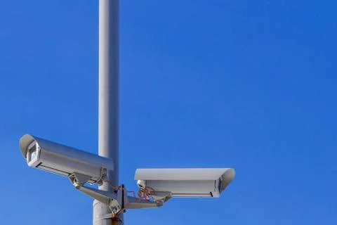 Two security cameras against the blue sky are monitoring. Stock Photos