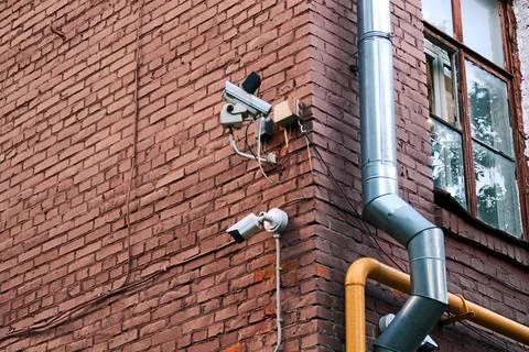 Two security cameras mounted on a red brick wall near a window Stock Photos
