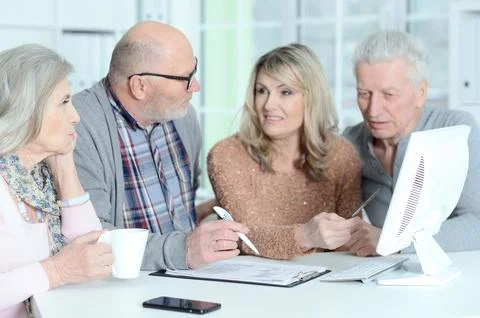 Two senior couples sitting at table and working with computer Stock Photos