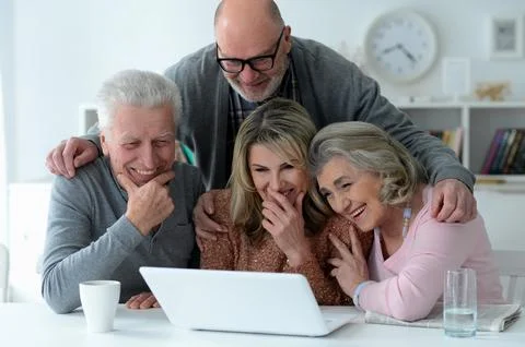 Two senior couples sitting at table and using laptop Stock Photos