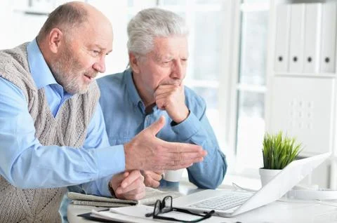 Two senior men sitting at table and using laptop Stock Photos