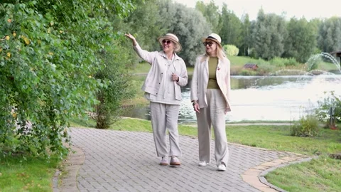 Two senior women friends walking together on park pathway, wearing light casual Stock Footage 318964853
