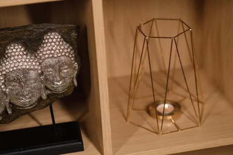 Two serene Buddha faces are set on a black stand beside a stylish gold candle Stock Photos