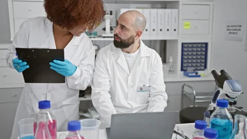 Two serious scientists at the lab, high-tech laptop and clipboard in hand, .. Stock Footage 268567831