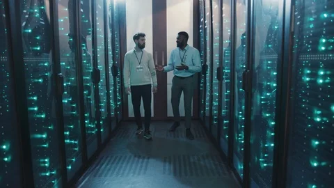 Two server technicians walking in rack server corridor talking about work Stock Footage 119081357