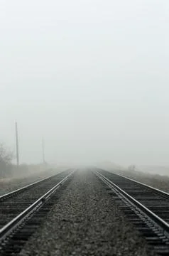 Two sets of straight train tracks disappearing into fog on a cold damp day. Stock Photos