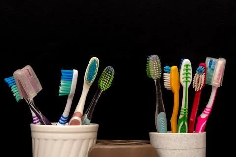 Two sets of toothbrushes in plastic cups on black background Stock Photos