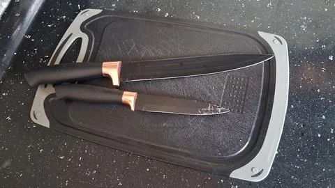 Two sharp black kitchen knives resting on a textured cutting board Stock Photos