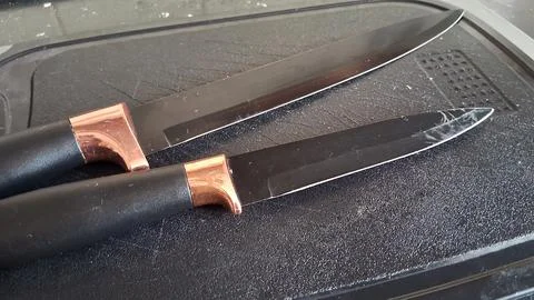 Two sharp black kitchen knives with copper handles resting together Stock Photos