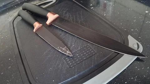 Two sharp black kitchen knives resting on a textured cutting board Stock Photos