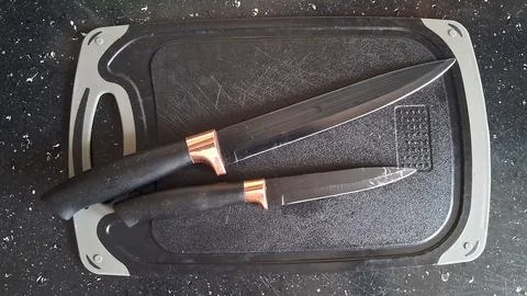 Two sharp kitchen knives with black handles resting on cutting board Stock Photos