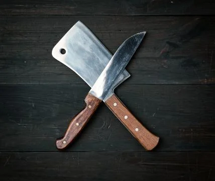 Two sharp knives lie on a brown wooden surface, kitchen items are crossed Foto stock