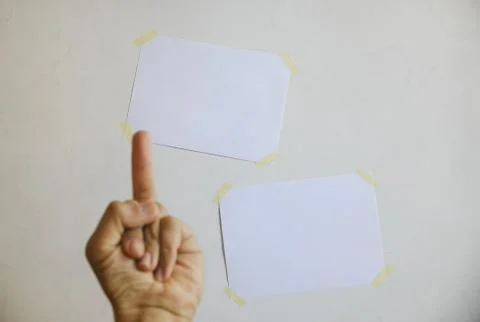 Two sheets of notes on the wall in front of which is a hand with a gesture of Stock Photos