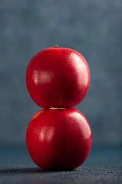 Two shiny red apples balanced vertically against a blue background. Stock Photos