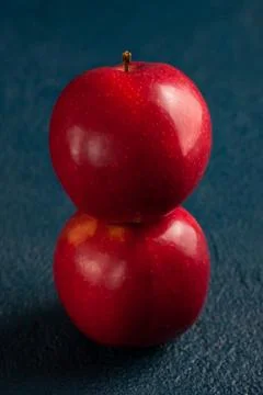Two shiny red apples balanced vertically a blue background. Top view Stock Photos