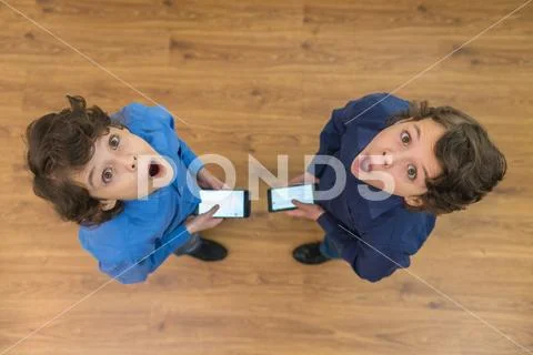 The two shocked twin stand with a phone. View from above Stock Photos