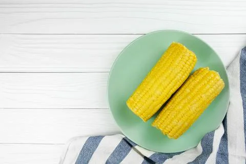 Two short boiled ears of corn on a green plate and a tea towel. Stock Photos