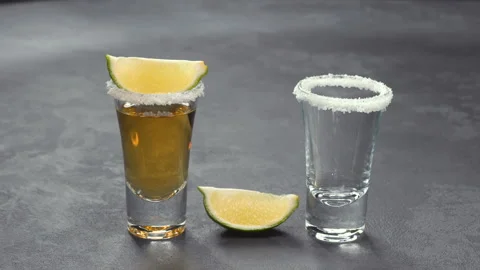 Two shot of cold gold tequila with white salt crystals in lime on a black wooden Stock Footage 98971342