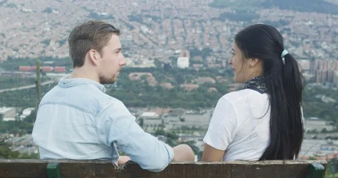 Two shot of young couple talking and overlooking city skyline on park bench Stock Footage 86149870