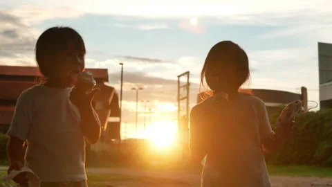 Two sibling sisters eattng sweet tasty ice cream outdoors at sunset.  Stock Footage 159794035