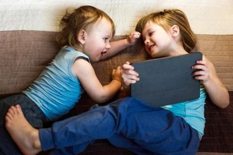 Two siblings laying on the bed with tablet Stock Photos