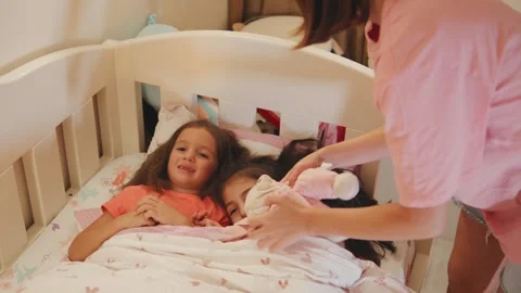 Two siblings lie in bed under a blanket while a caregiver gently brushes their Stock Footage 330749973