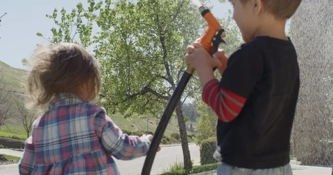 Two siblings, playing together spraying water in the yard, shot on RED EPIC Stock Footage 105375784