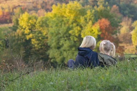 Two siblings sit hugging on grass on autumn landscape background. Carefree .. Stockfoto's