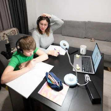 Two siblings study at home one writes while the other helps with tech in a wa Stock-Fotos