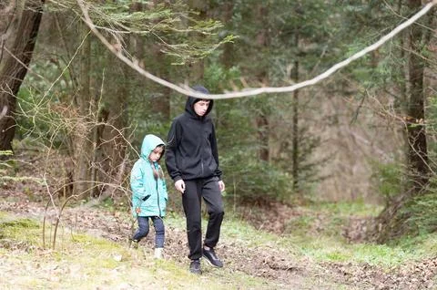 Two siblings wander through a lush forest, dressed in hooded jackets, enjoyin Stock Photos
