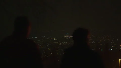 Two Silhouettes Of People Standing On Top Of Hill, Overlooking City Night Stock Footage 267010945