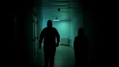Two silhouettes in protective suits walk along a dark corridor. 스톡 동영상 314339554