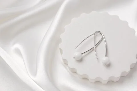 Two silver earrings with white agate on a concrete podium on silk. Beautifu.. Stock Photos