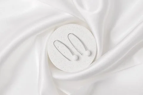 Two silver earrings with white agate on a concrete podium on silk. Beautifu.. Stock Photos