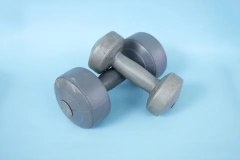 Two silver plastic dumbbells isolated on a blue background Stock Photos