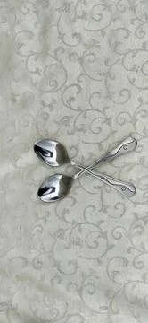 Two silver spoons crossed on a patterned fabric background Stock Photos