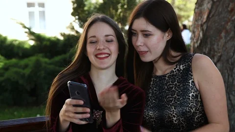 Two Simpering girlfriends in the Park Laughing Watching a smartphone Hugging Vidéo 114173097