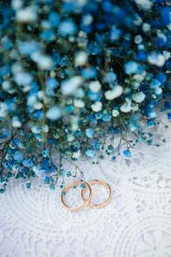 Two simple gold wedding bands rest on a lace surface beside a bouquet of bl.. Фото