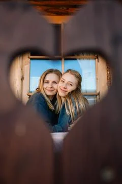 Two sisters are hugging each other, seen through heart shaped hole in wooden Stock Photos