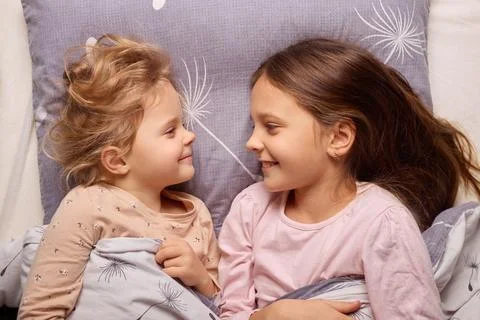 Two sisters are lying in bed, smiling and enjoying each other's company. Th.. Stock Photos