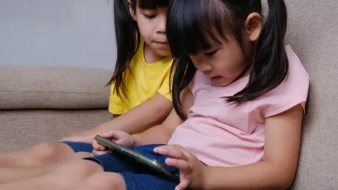 Two sisters are playing online games on smartphones sitting on the sofa at home. Stock Footage 170878993