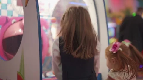 Two sisters are playing in shop center. A gaming machine in form of pink pig. 库存影片 144732363