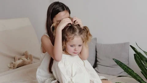 Two sisters are sitting on a bed in a bright bedroom. The older sister is Stockbeeldmateriaal 336459805