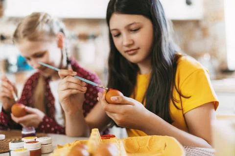 Two sisters are sitting at the table and painting Easter eggs in different Foto stock