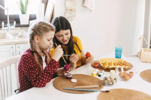 Two sisters are sitting at the table and painting Easter eggs in different Foto stock