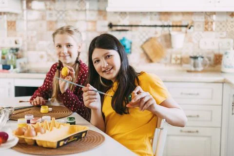 Two sisters are sitting at the table and painting Easter eggs in different Foto stock