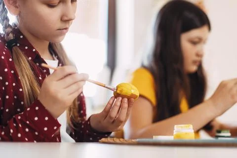 Two sisters are sitting at the table and painting Easter eggs in different Stock Photos
