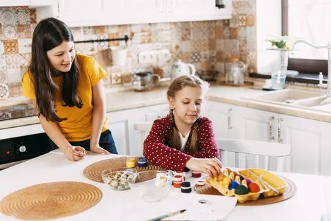 Two sisters are sitting at the table and painting Easter eggs in different Stock Photos