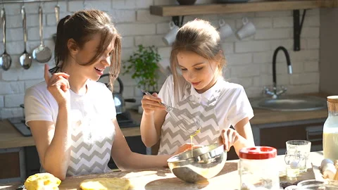 Two sisters cooking together. Elder sister showing younger how to mix eggs. Stock Footage 106239329